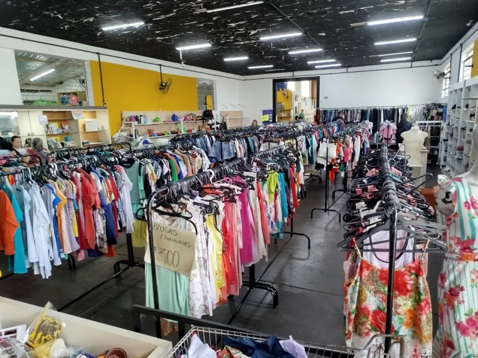 Corredor do salão do bazar com araras de roupas coloridas e manequins, sob um forro escuro e manchado
