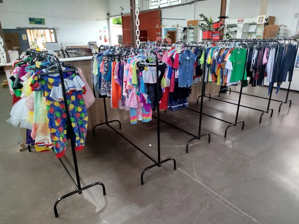 Salão do bazar com araras de roupas, fantasias coloridas à esquerda e algumas araras ainda vazias