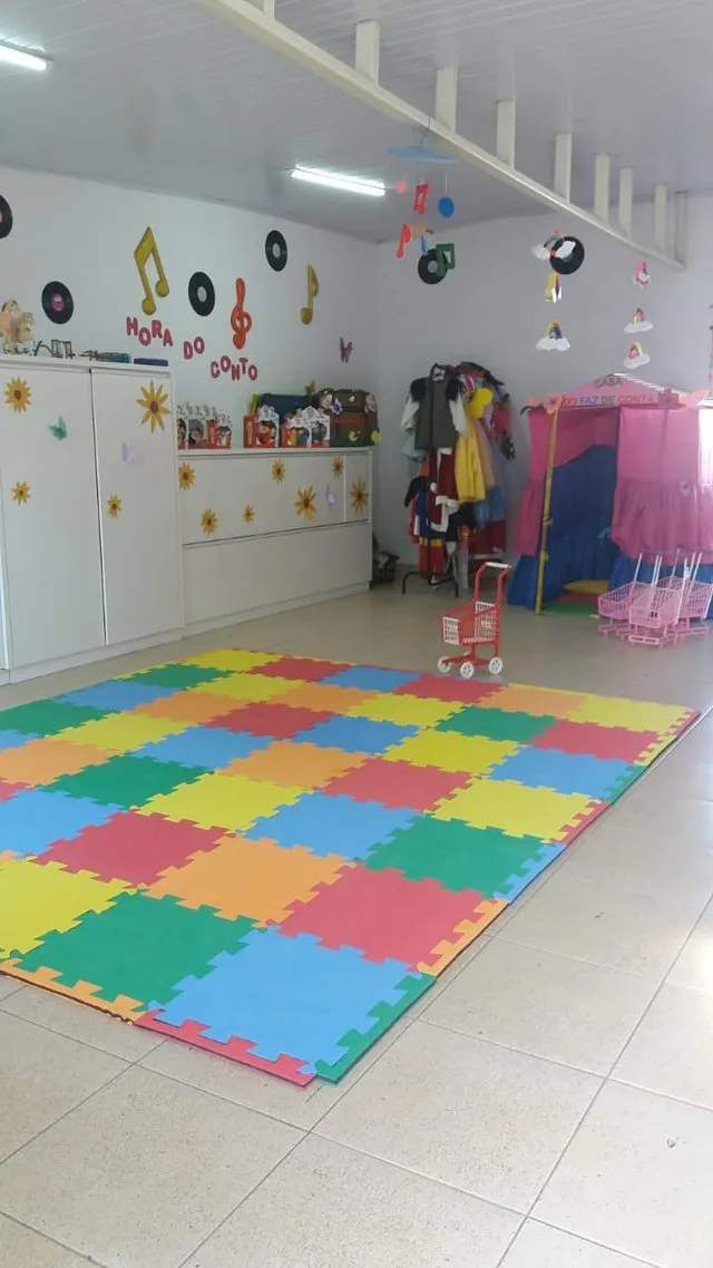 Sala multiuso com tapete de tatame colorido, cantinho da Hora do Conto e Casa do Faz de Conta
