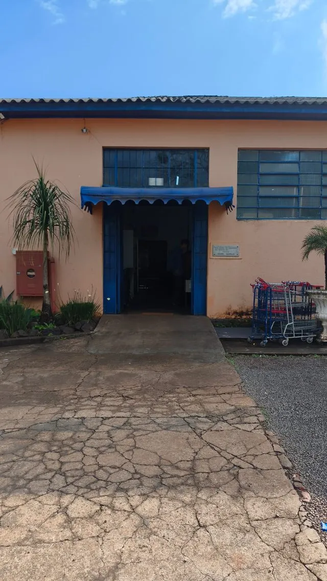 Entrada do Bazar Beneficente, com toldo azul e carrinhos de compra ao lado